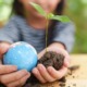 environmental project grants and education grants: little girl holding globe and newly sprouted tree in soil