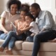family services, economic mobility and healthy homes grants: young black family on couch laughing while looking at tablet device