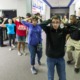 School shootings drill: Line of several teens with hands up behind heads stand in side building hallway protected by armed police