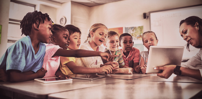 iCivics curricylum: Teacher showing tablet computer to several elementary students sitting at large classroom yable